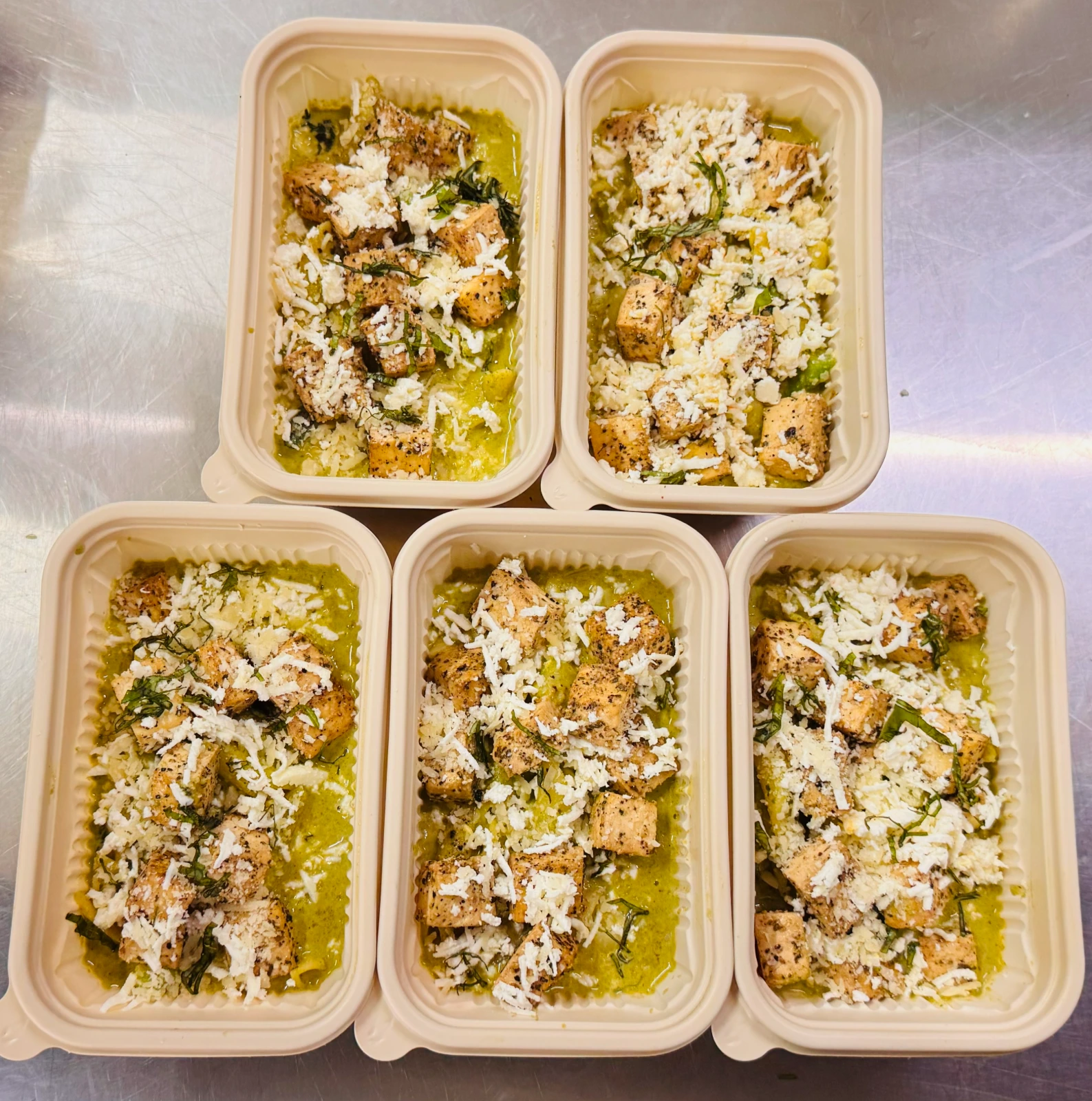 Five eco-friendly meal prep containers filled with Herb-Grilled Chicken Saag Ricotta Pasta topped with grated cheese at Carb Theory in Bangalore.